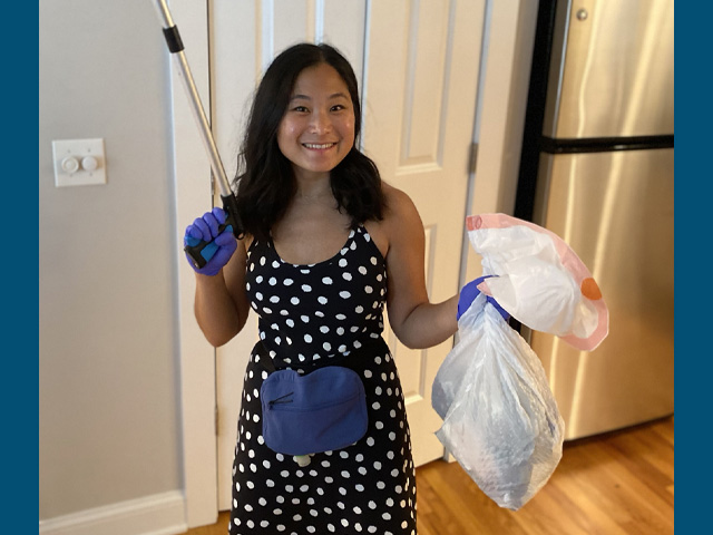 Susan Pak stands in a kitchen smiling, holding a bag of trash and a grabber.