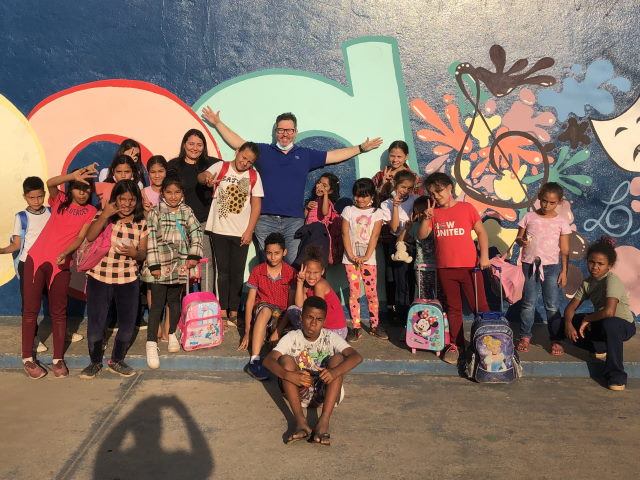 Alexandre poses with a large group of children in front of a painted wall. 