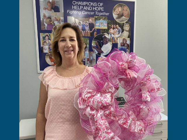 Cheryl posing with a pink wreath made of ribbons to signify breast cancer awareness.