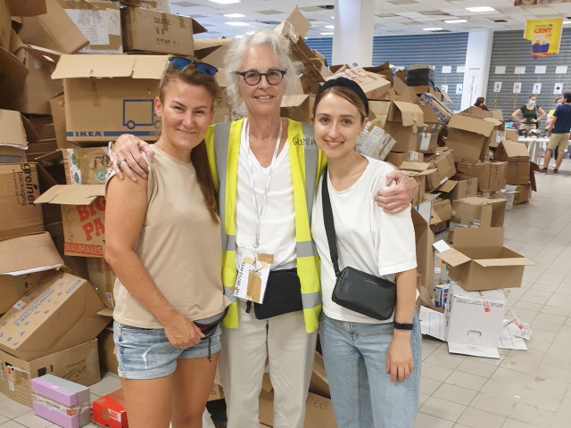 Katarzyna and two other women posing in front of tall piles of cardboard boxes.