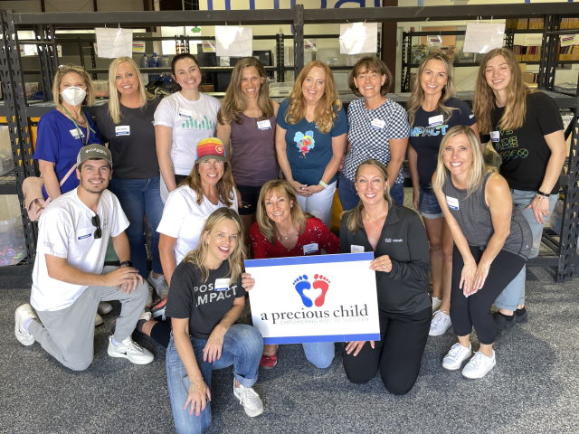 A large group of people pose for a picture with a sign reading a precious child.