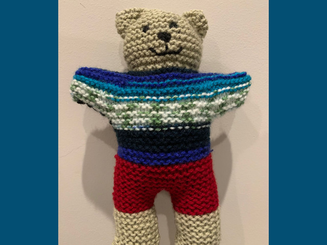 A knitted teddy bear with a muti-colored sweater.