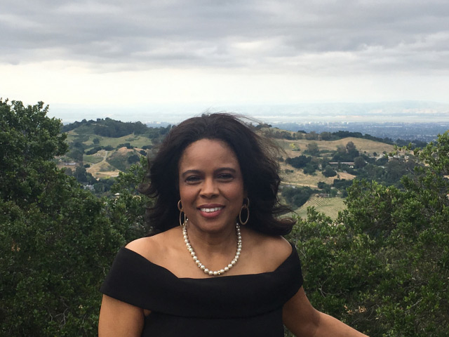 Aleta smiles and poses in front of green hills in California