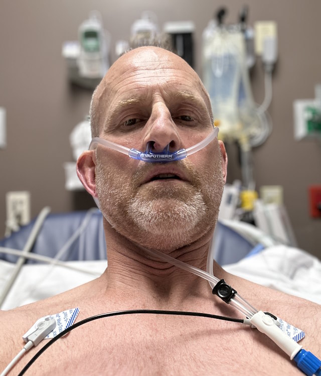 John in a hospital bed with an oxygen tube in his nose.