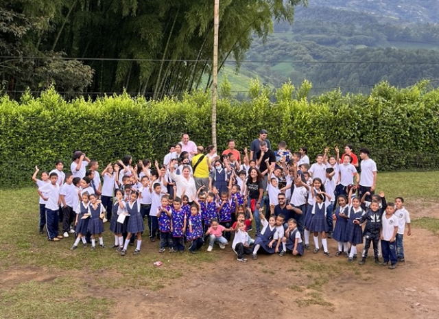 A large group of  volunteers and school children smiling and waving at the camera.