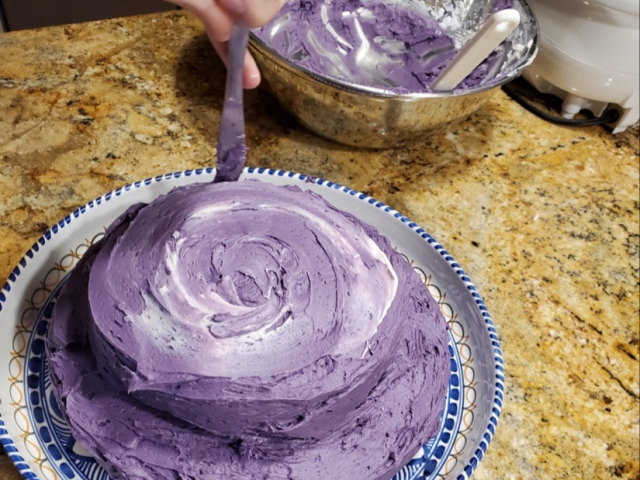 A person spreading a vibrant purple ube frosting on a cake.