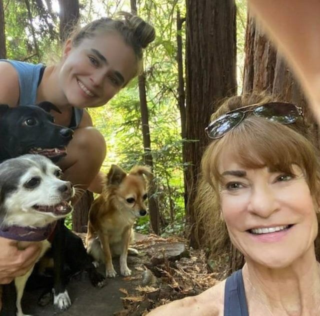 Cathryn takes a selfie in a forest with her daughter and three dogs. 