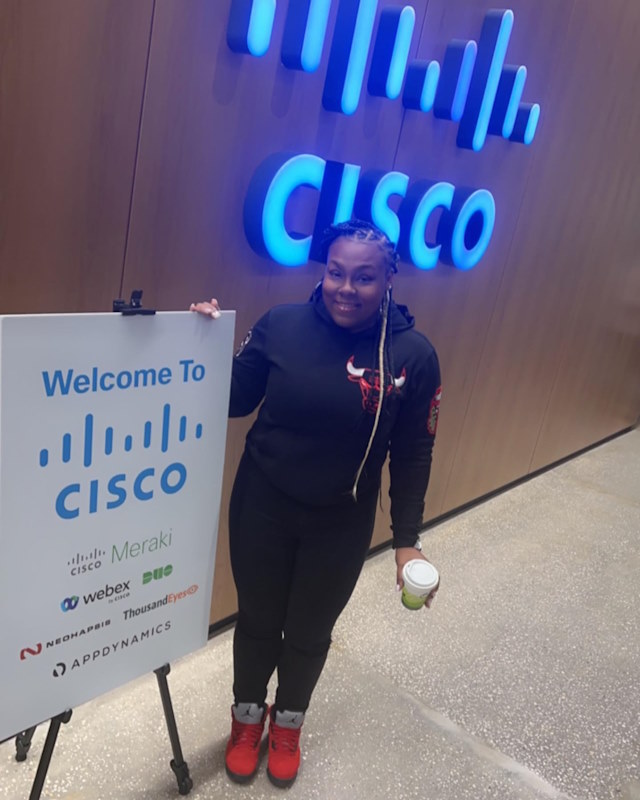 Andrea smiles in an entrance to a Cisco office wearing a Chicago Bulls sweatshirt.