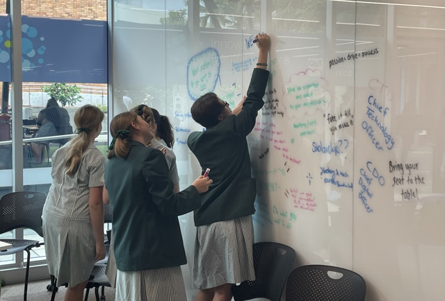 Four girls in school uniforms  writing on a whiteboard in Brisbane. 