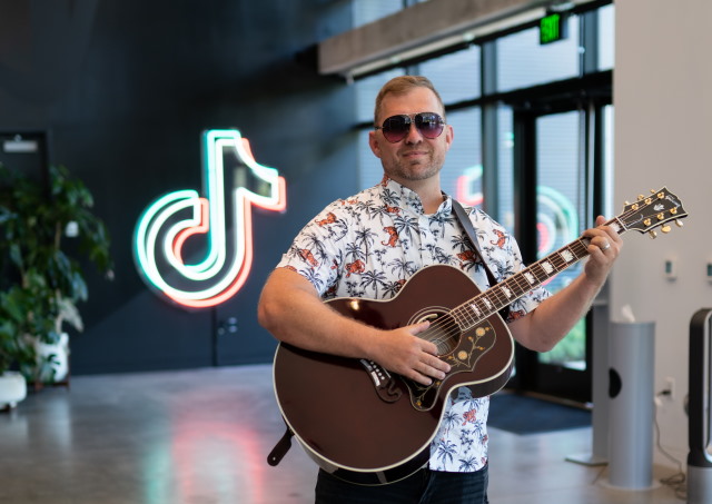 Luke Reynolds holding a guitar in an office building lobby