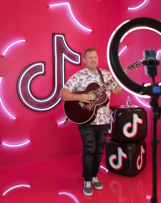 Luke holding a guitar in front of neon pink TikTok logo