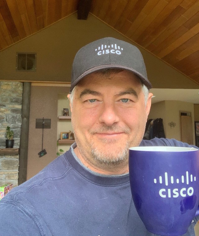 Brett wearing a Cisco hat and holding a Cisco mug.