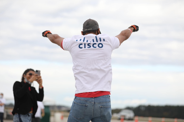 A person outdoors wearing a Cisco shirt, raising their arms in the air