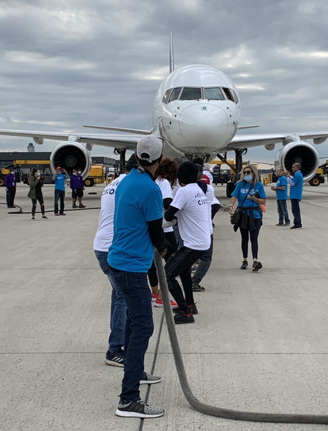 Group of people facing pulling on a large rope tied to the front of a cargo plane.