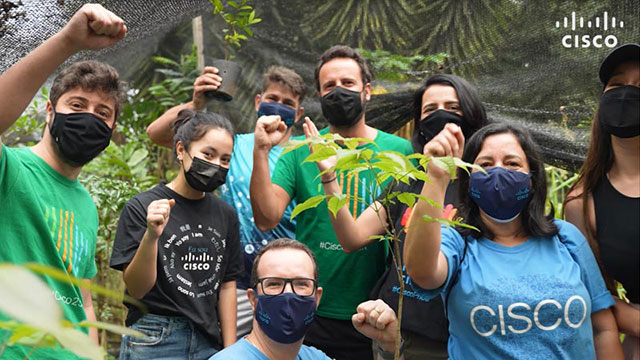 The Cisco Green Team Brazil pose  with their fists raised surrounded by plants.