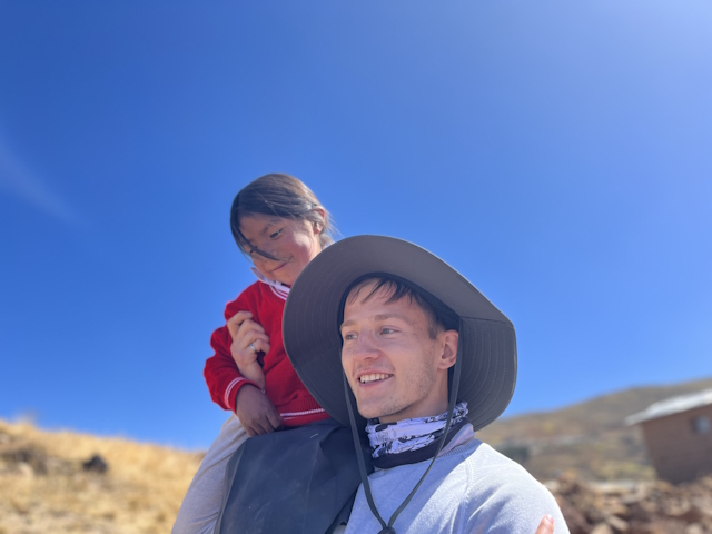 Ryan Holt outside in a hat with a smiling child in a red sweater sitting on his shoulder.