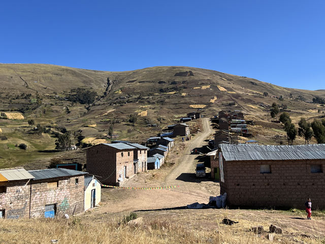 A small group of brown houses line a dirt road on a hillside.