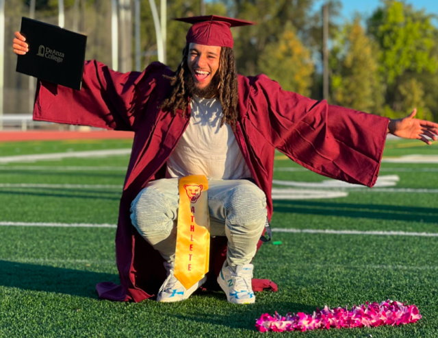 Covenant House resident Pazz ecstatically poses on a football field in his red graduation cap and gown.