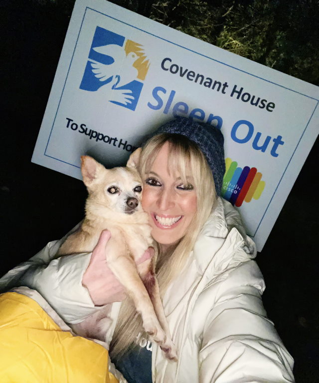 Rachael smiles with her dog Jack in front of a Sleep Out poster.