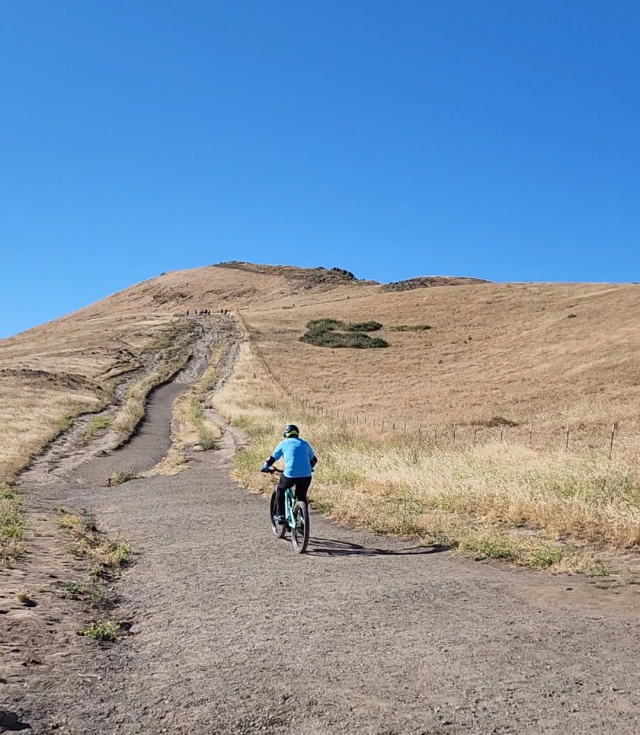 Rohan on his bike, riding up the trail with Mission  Peak ahead of him.