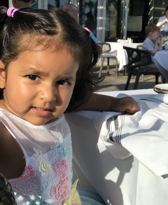 A toddler Fiona sits at a  restaurant table.