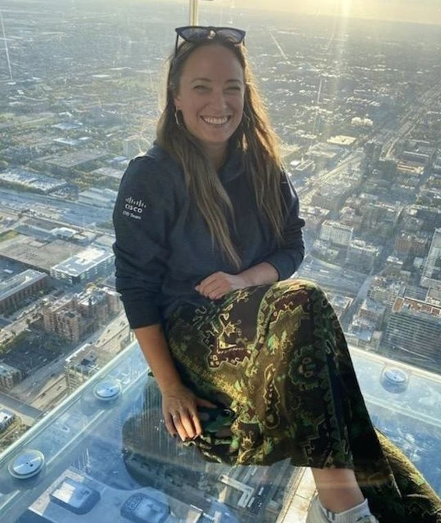 The author sits in a glass enclosure with the Chicago skyline visible around and below her.